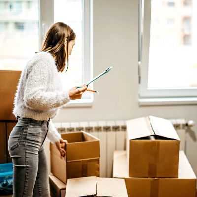 image shows a young woman with a clipboard looking over packed boxes